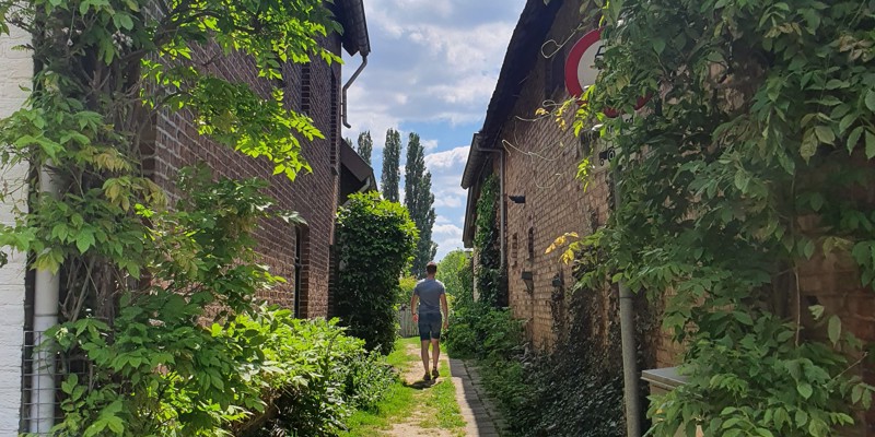 Een jongeman wandelt tussen twee huizen door over een wandelpad naar het Vrouwenbos